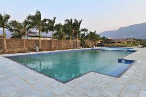 a swimming pool in a yard with palm trees at The Kanila Resort in Karjat