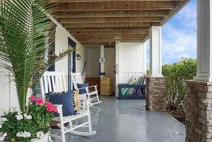 un porche con sillas blancas y flores en Carolina Beach Inn, en Carolina Beach