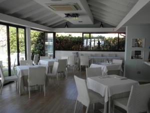a restaurant with white tables and chairs and windows at Baia Santa Maria in Cittadella del Capo