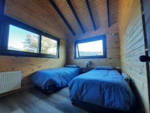 2 Betten in einem Holzzimmer mit 2 Fenstern in der Unterkunft Refugio de montaña en pleno centro Malalcahuello. in Malalcahuello