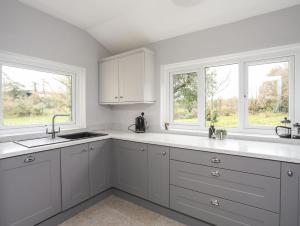 a white kitchen with white cabinets and two windows at Gorwel in Llanallgo