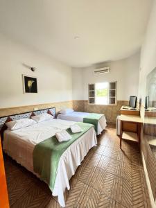 a bedroom with two beds and a desk and a television at Hotel Fazenda Pousada da Serra in Goianésia