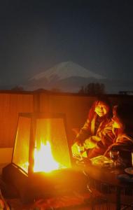 uma mulher sentada ao lado de uma lareira numa sala em ヴィラ山間堂Panorama Villa BBQ Bonfire Fuji view Annovillas Sankando em Fujikawaguchiko