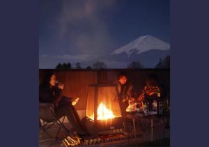 tres personas sentadas alrededor de un fuego con una montaña en el fondo en ヴィラ山間堂Panorama Villa BBQ Bonfire Fuji view Annovillas Sankando, en Fujikawaguchiko