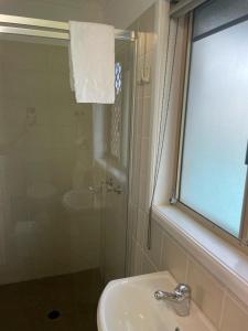 La salle de bains est pourvue d'un lavabo, d'une douche et d'une fenêtre. dans l'établissement Kyamba Court Motel, à Mooloolaba