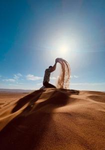 Brija的住宿－Tinfou desert camp，站在沙漠中,有太阳在后面的人