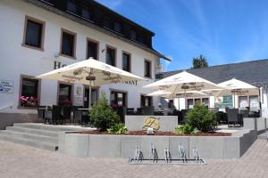 Hotel Restaurant Haus Zwicker في Bleialf: مطعم بطاولات ومظلات امام المبنى