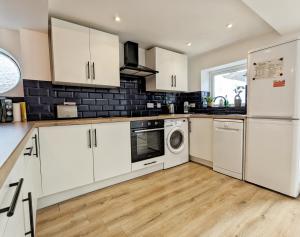 a kitchen with white cabinets and a washer and dryer at Blue Horizon Holiday Cottage - 4 Minute Walk to the Beach in Weymouth