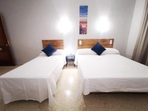 two beds in a room with white sheets and blue pillows at Hotel Don Cándido in Puerto de la Cruz