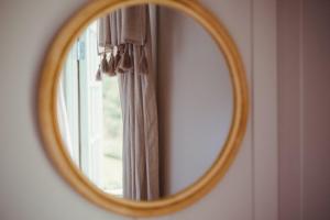 a round mirror on a wall with a curtain at Toad Hall Lodges - Luxury Eco Lodges Near Southwold! in Wangford