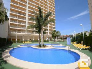 a swimming pool with a palm tree and a large building at Apartamento Ambar Beach 18D - Grupo Turis in Calpe