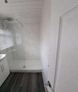 a white bathroom with a shower and a wooden floor at 1 Bed Apart in Dowlais
