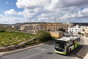 a green and white bus driving down a street at Seaside Flat with Scenic Country Views in Mellieħa