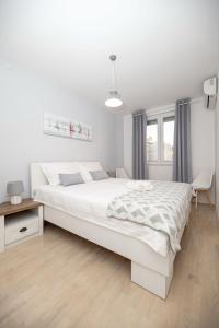 a white bedroom with a large bed and a desk at Apartment Sundowner in Zadar