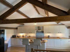 a large kitchen with white cabinets and wooden beams at 2 Malt Kiln Cottages in Grizebeck