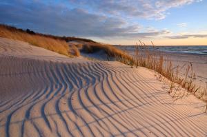 una playa de arena con olas en la arena y el océano en Jantar Medical Spa, en Dziwnówek