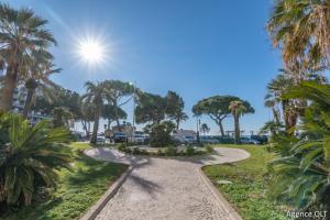 a walkway through a park with palm trees and the sun at CENTER BAY in Juan-les-Pins