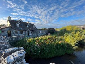 a stone house next to a river with flowers at Aille River Tourist Hostel Glamping Doolin in Doolin