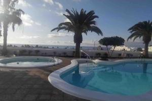 uma grande piscina com palmeiras e o oceano em Casaloé em Puerto del Carmen