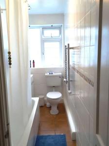 a bathroom with a toilet and a tub and a window at 2 Bed Flat Near Station with Parking&Comgarden in Sutton