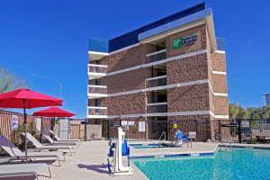 una piscina con sillas y sombrillas frente a un hotel en Holiday Inn Express & Suites Phoenix - Tempe, an IHG Hotel en Tempe