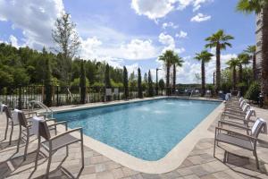 a swimming pool with chairs and palm trees at Courtyard by Marriott Orlando South/Grande Lakes Area in Orlando