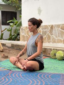 una mujer sentada en el suelo en una pose de yoga en Green's Nungwi, en Nungwi