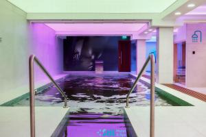 an indoor swimming pool in a building with purple lighting at Stil Motel & Spa in Tăşnad