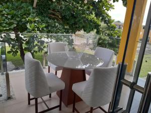 een glazen tafel en witte stoelen op een balkon bij Apartamento pé na areia in Porto Seguro