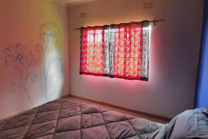 1 dormitorio con ventana y cortina roja en Artist Villa in a Beautiful Yard en Chilanga