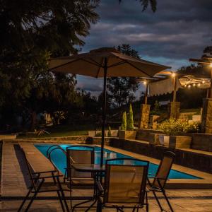 una mesa con sillas y una sombrilla junto a la piscina en Casa de Campo La Montaña en Tarija