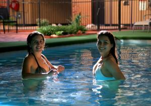 two women are swimming in a swimming pool at Stay at Alice Springs Hotel in Alice Springs