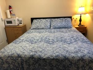 a bedroom with a bed with a blue comforter and a microwave at Shady Willow Guest House -Coach house & Privet Small Compact Rooms with separate entrance in Chilliwack