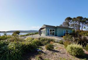 a small blue house on the shore of a lake at Waterfront 'Jemadda' Family Lodge in Bream Creek