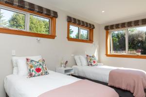 two beds in a room with two windows at Anam Cara Gardens luxury Villa in Otaki