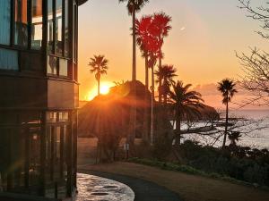 a sunset over the ocean with palm trees and a building at Shimoda Tokyu Hotel in Shimoda