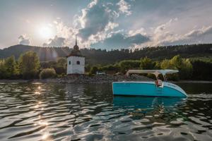 a boat in the water with a church in the background at Chalupa u rybára s Wellness a detským ihriskom in Liptovský Trnovec
