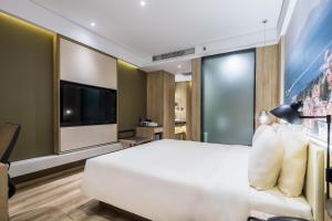 Atour Hotel Qingdao Fuzhou Road Sakura Town في تشينغداو: غرفة نوم بسرير ابيض كبير وتلفزيون بشاشة مسطحة