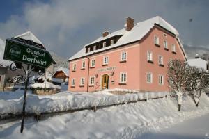 ein großes rosafarbenes Gebäude mit einem Schild im Schnee in der Unterkunft Gasthof Dorfwirt in Ardning