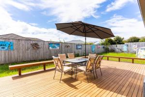 une table et des chaises avec un parasol sur une terrasse dans l'établissement Summertime Bliss - Mangawhai Heads Holiday Home, à Mangawhai