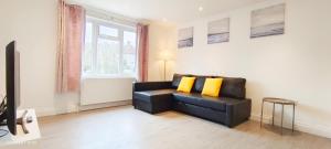 a living room with a black leather couch and yellow pillows at Green Garden in Northwest London in London