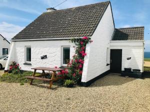 ein kleines weißes Gebäude mit einem Picknicktisch und Blumen in der Unterkunft Doonbeg Holiday Cottages in Doonbeg