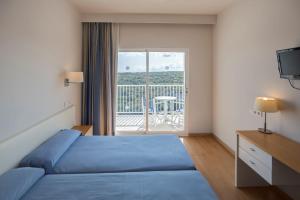 a bedroom with a blue bed and a balcony at Seth Playa Azul in Cala'n Porter