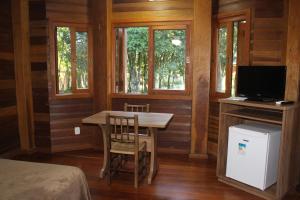 Habitación con mesa, TV y ventanas. en Pousada Floresta Negra, en Canela