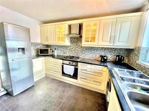 a kitchen with white cabinets and a stainless steel refrigerator at The HK House - Family Friendly Near To Blenheim Palace & Oxford City Centre in Kidlington