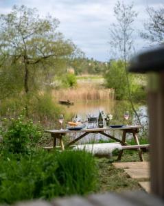 a picnic table next to a river with wine glasses at Lakeside Eco Lodge- 'Heron' in Bishampton