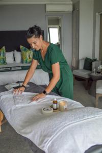 a woman making a bed in a hotel room at African Oceans Manor on the Beach in Mossel Bay