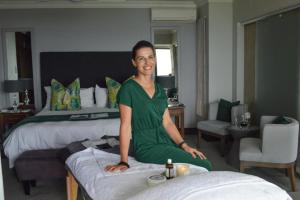 kobieta siedząca na łóżku w pokoju hotelowym w obiekcie Bay Lodge on the Beach w mieście Mossel Bay