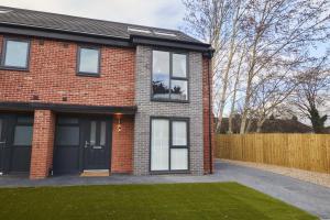 a red brick house with a wooden fence at Homebird Property - The Willows in Leeds