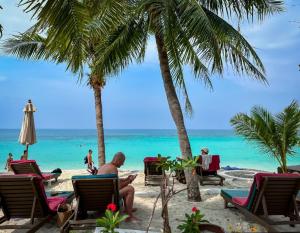 a man sitting on a beach with palm trees and the ocean at Green Papaya Beach Resort, Koh Phangan in Salad Beach